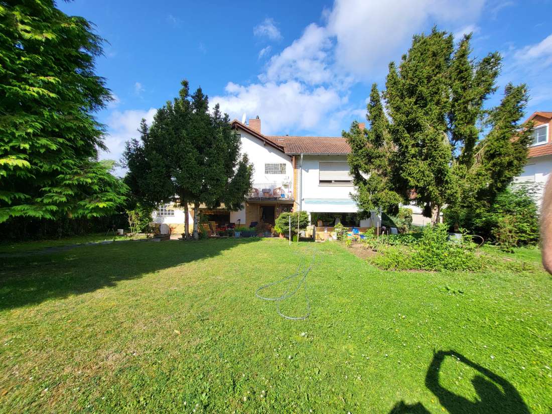 Gartenseite des Hauses mit Terrasse und Balkon, davor Rasenfläche mit altem Baumbestand